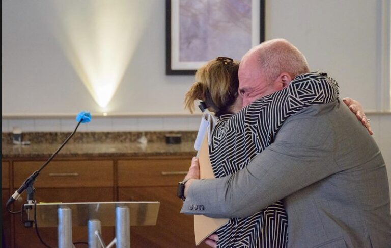 Two Clusterbusters conference attendees embracing near a podium.
